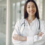 Crop doctor in medical uniform with stethoscope standing in clinic corridor