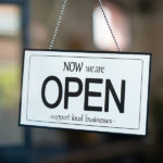 Reopening of a small business activity after the covid-19 emergency, ended the lockdown and quarantine. A business sign that says now we are open support local businesses hang on door at entrance.